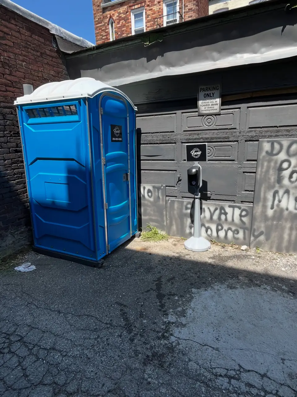 Blue porta potty placed on asphalt next to a building