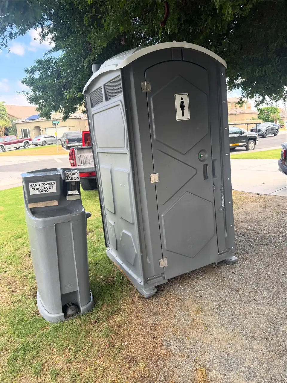 Gray portable toilet next to a foot-pump hand wash station on a lawn