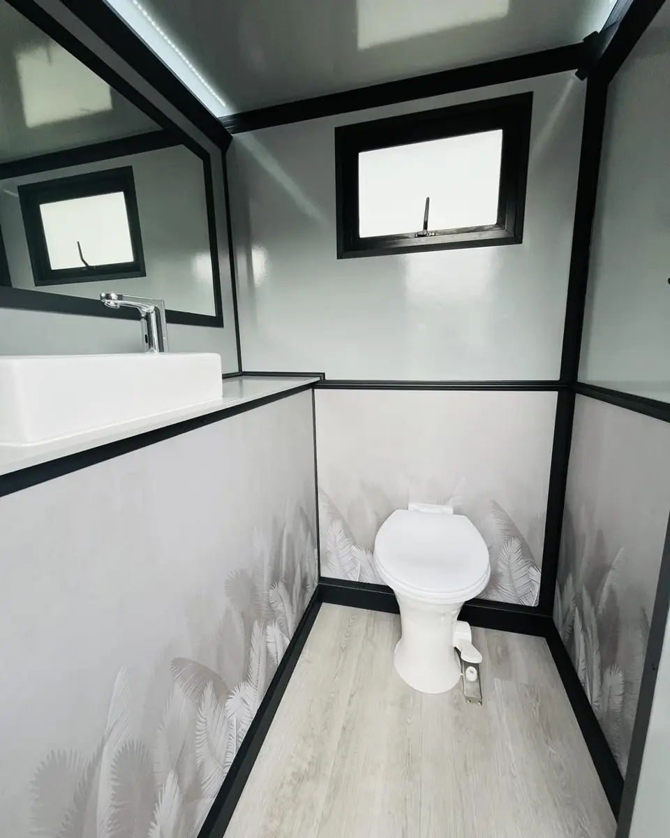 Inside a restroom trailer stall with a porcelain toilet, vanity counter and window