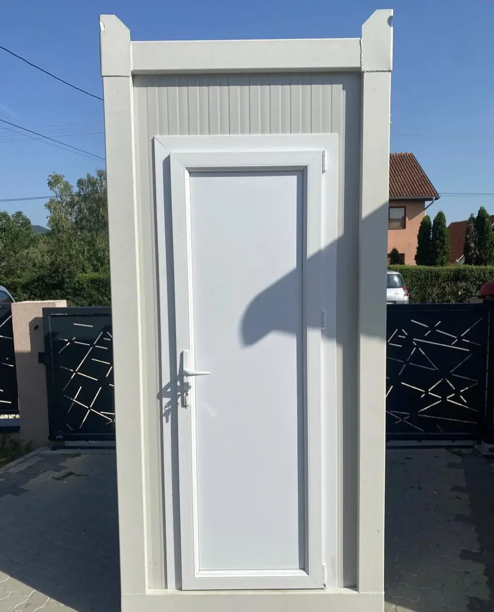 White single restroom cabin with paneled door outdoors