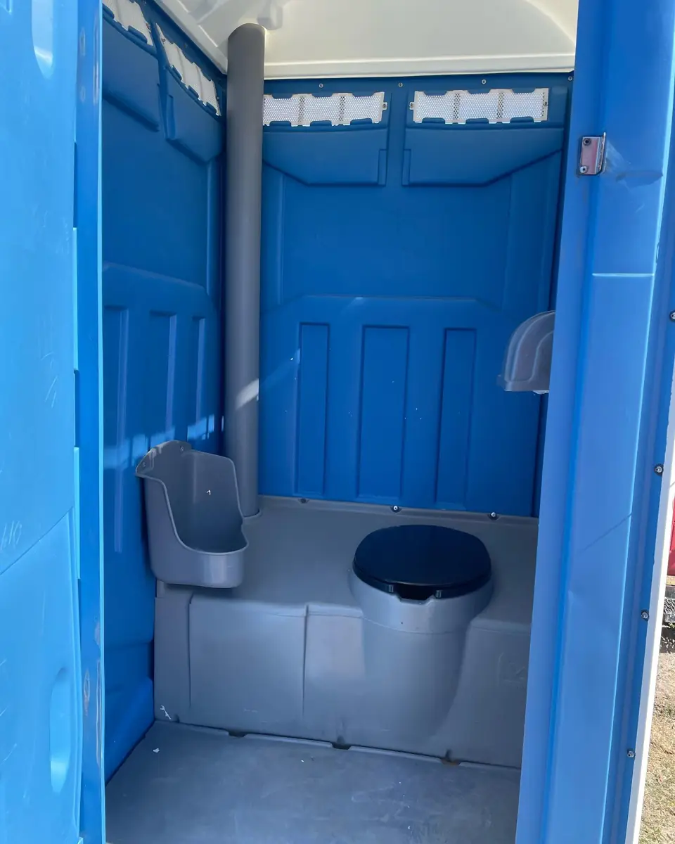 Inside a standard blue porta potty showing toilet, urinal and paper holders