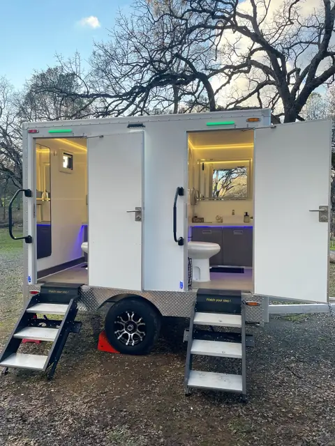 Two-stall restroom trailer with doors open on a grass lawn