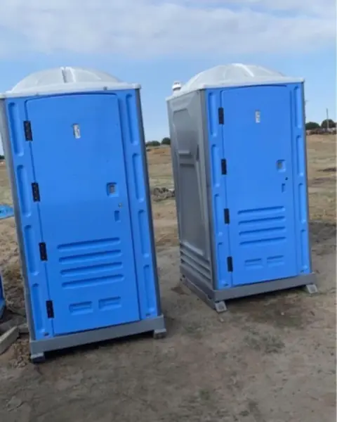 Two blue standard porta potties standing side by side on open ground
