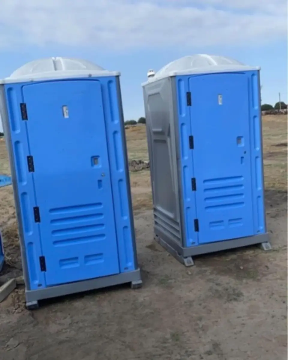 Two blue standard porta potties standing side by side on open ground